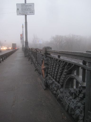 Soviet metalwork on bridge railing under a Ukrainian/English dual-language sign; official signs don't use Russian.