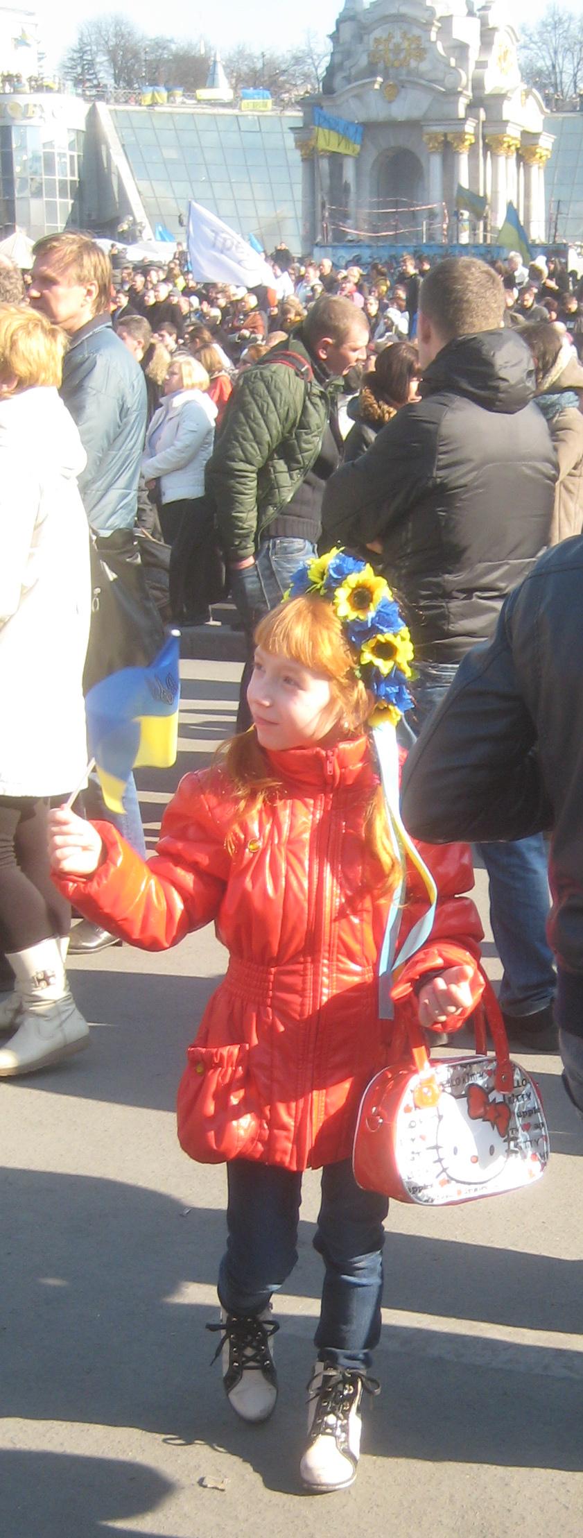 A girl on the Maidan with Euromaidan (and Hello Kitty) paraphernalia, the Independence Monument behind her